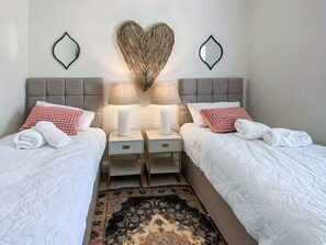 Une chambre d’hôtel avec deux lits, une décoration murale en forme de cœur, deux lampes de chevet et un tapis à motifs.