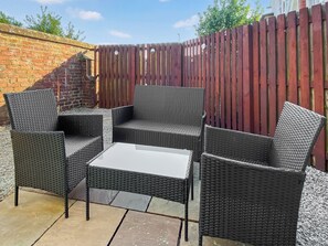 A patio area with wicker furniture, including chairs and a table, set against a brick wall and a wooden fence. - The Guards Quarters - UK47594 (Silloth)