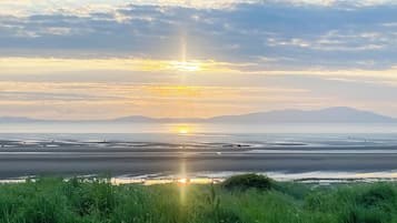 A coastal landscape with a sunset over the water, mountains in the distance, and grassy foreground.