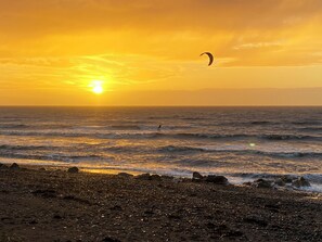 A beach at sunset with a kite surfer in the distance.