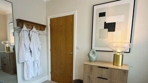 A hallway with a wooden door, a mirror, a white robe rack, a framed abstract painting, a lamp, and a storage unit.