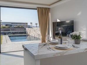 A modern dining area with a pool view, marble countertops, and a bottle of wine. - Lithos Luxury Resort - Pelagos (Anissaras)