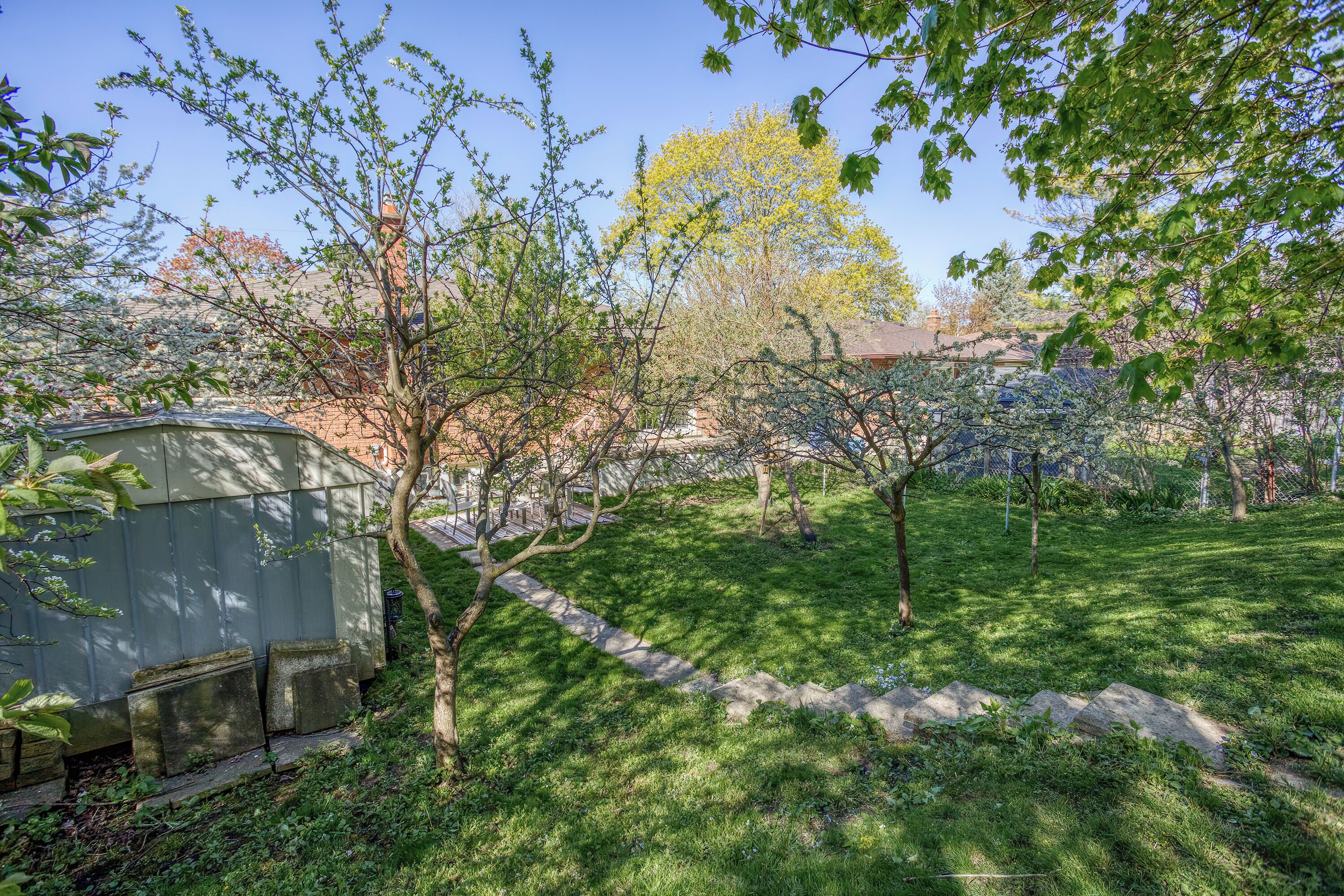 Ein Garten mit einem Gartenhaus, einem Kiesweg und verschiedenen Bäumen.