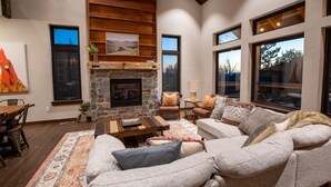 A modern living room with a stone fireplace, large windows, and a cozy seating area.