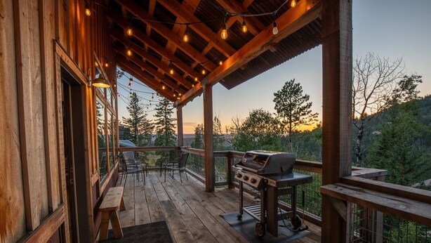 A wooden deck with a grill and seating, overlooking a forested area.