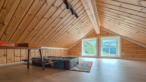A spacious attic room with wooden slats on the ceiling, a foosball table, and a large window with a view of greenery. - Awesome home in Norheimsund with WiFi (Norheimsund)
