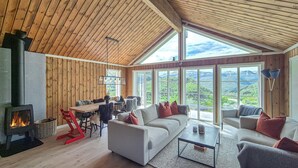 A spacious living room with a fireplace, a sofa, a coffee table, and large windows offering a view of the outdoors. - Awesome home in Norheimsund with WiFi (Norheimsund)