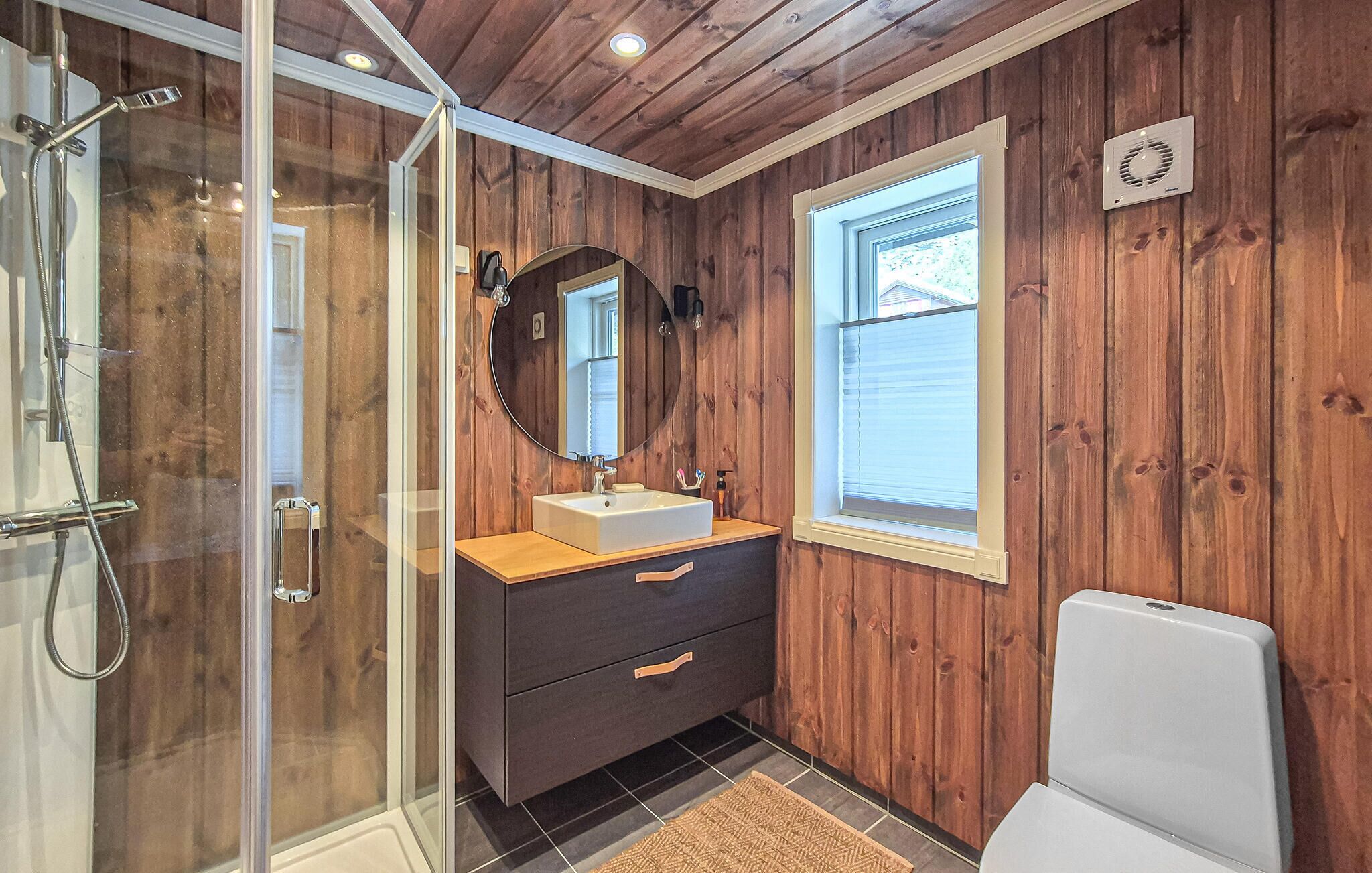 A bathroom with wooden panel walls, a glass shower enclosure, a sink with a mirror, and a toilet.