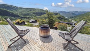 A wooden deck with two striped chairs and a metal container, overlooking a valley with houses and greenery. - Awesome home in Norheimsund with WiFi (Norheimsund)