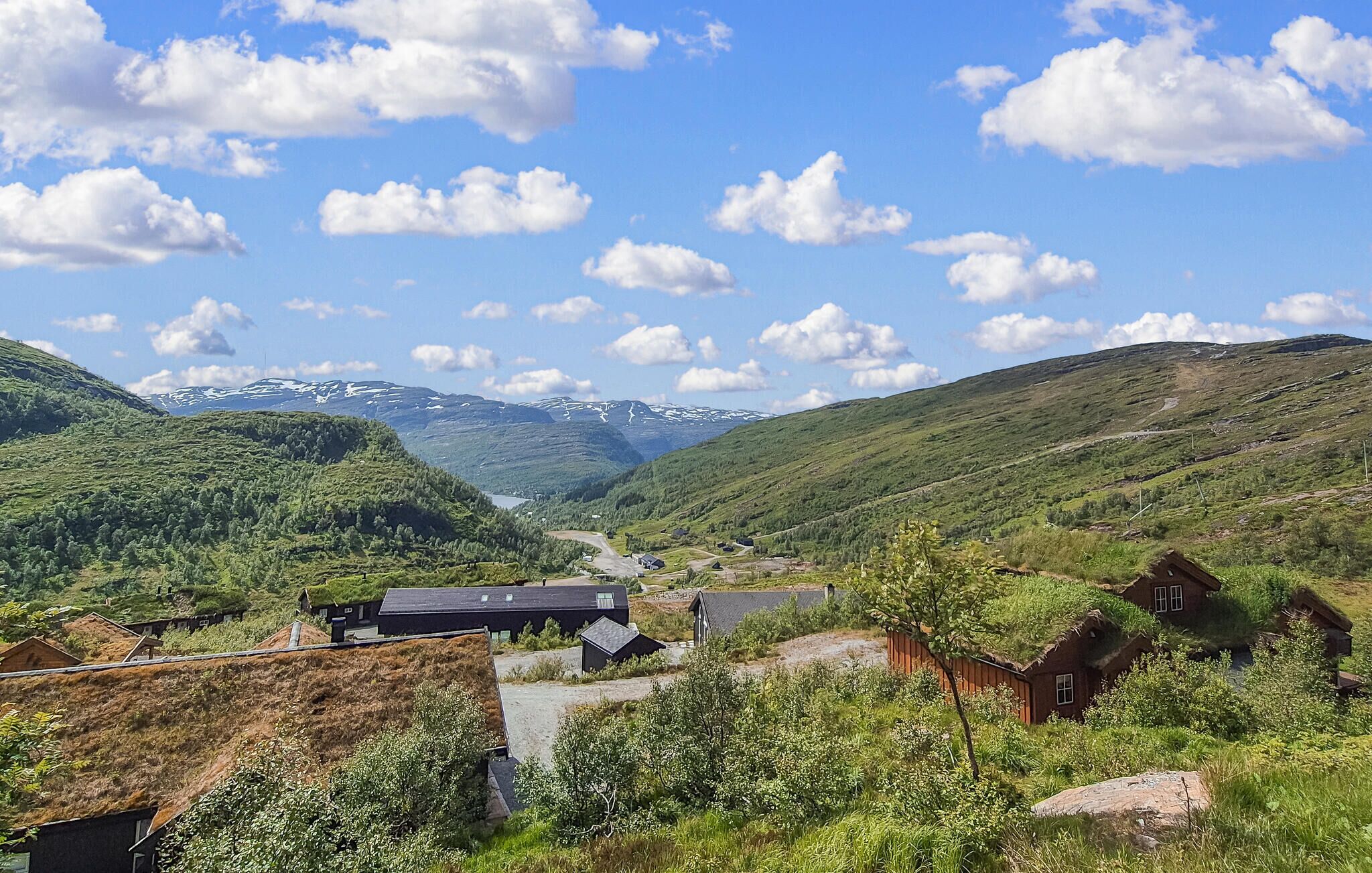 A rural village with traditional houses, a winding road, and a valley with mountains in the background.