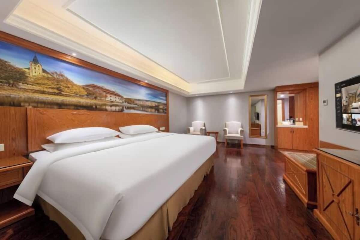 A hotel room with a large bed, a painting on the wall, a TV, and wooden furniture.