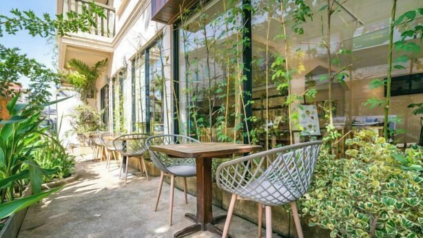 An outdoor cafe with tables and chairs, surrounded by greenery and a building with large windows. - Bakong Hotel (Siem Reap)