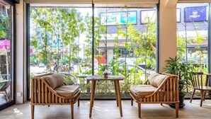 A room with a large window, two wooden chairs, a small table, and a potted plant. - Bakong Hotel (Siem Reap)