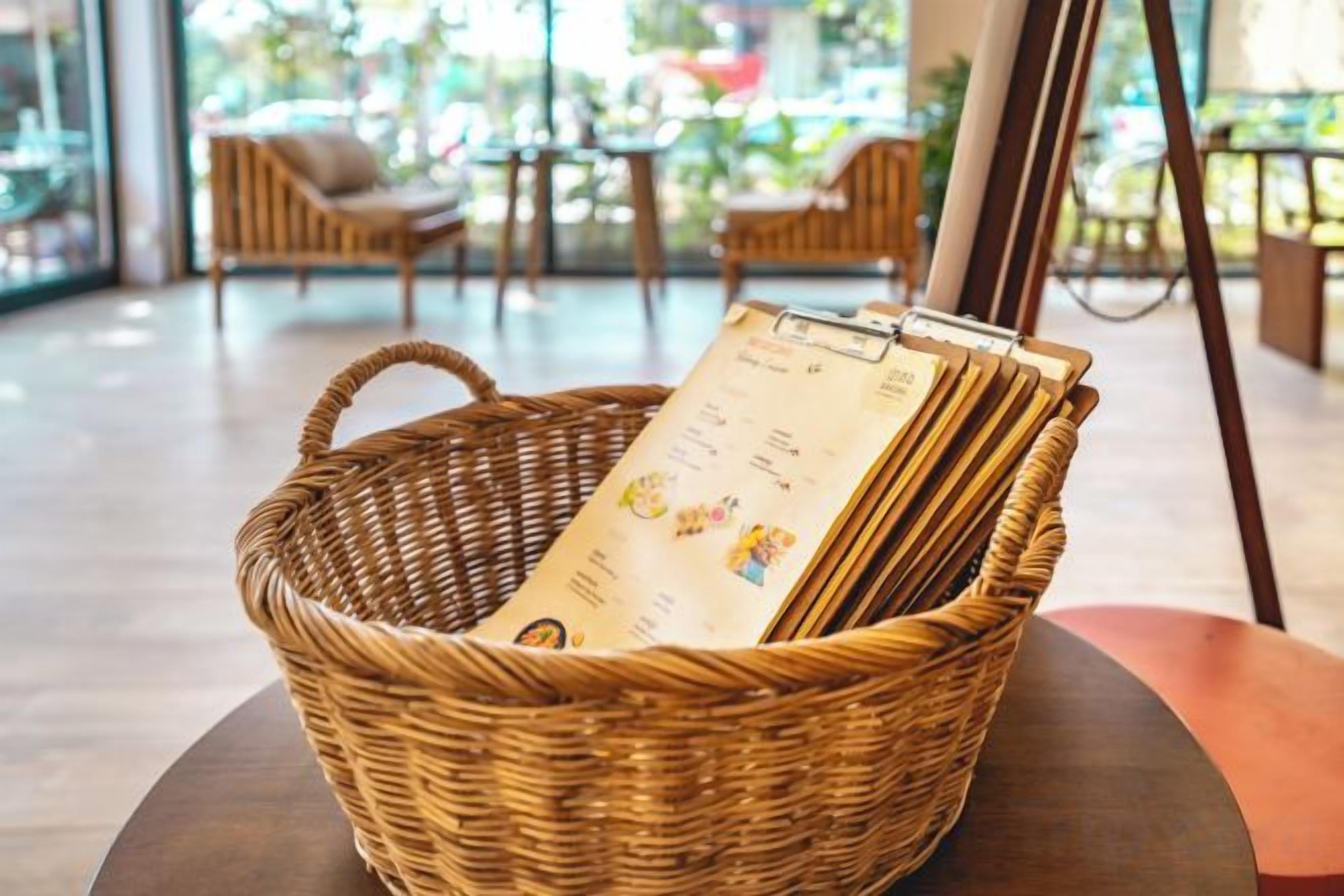 A wicker basket with menus on a table in a cafe setting.