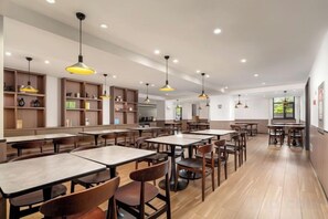 Um restaurante amplo, com várias mesas e cadeiras, iluminação pendente e piso de madeira.