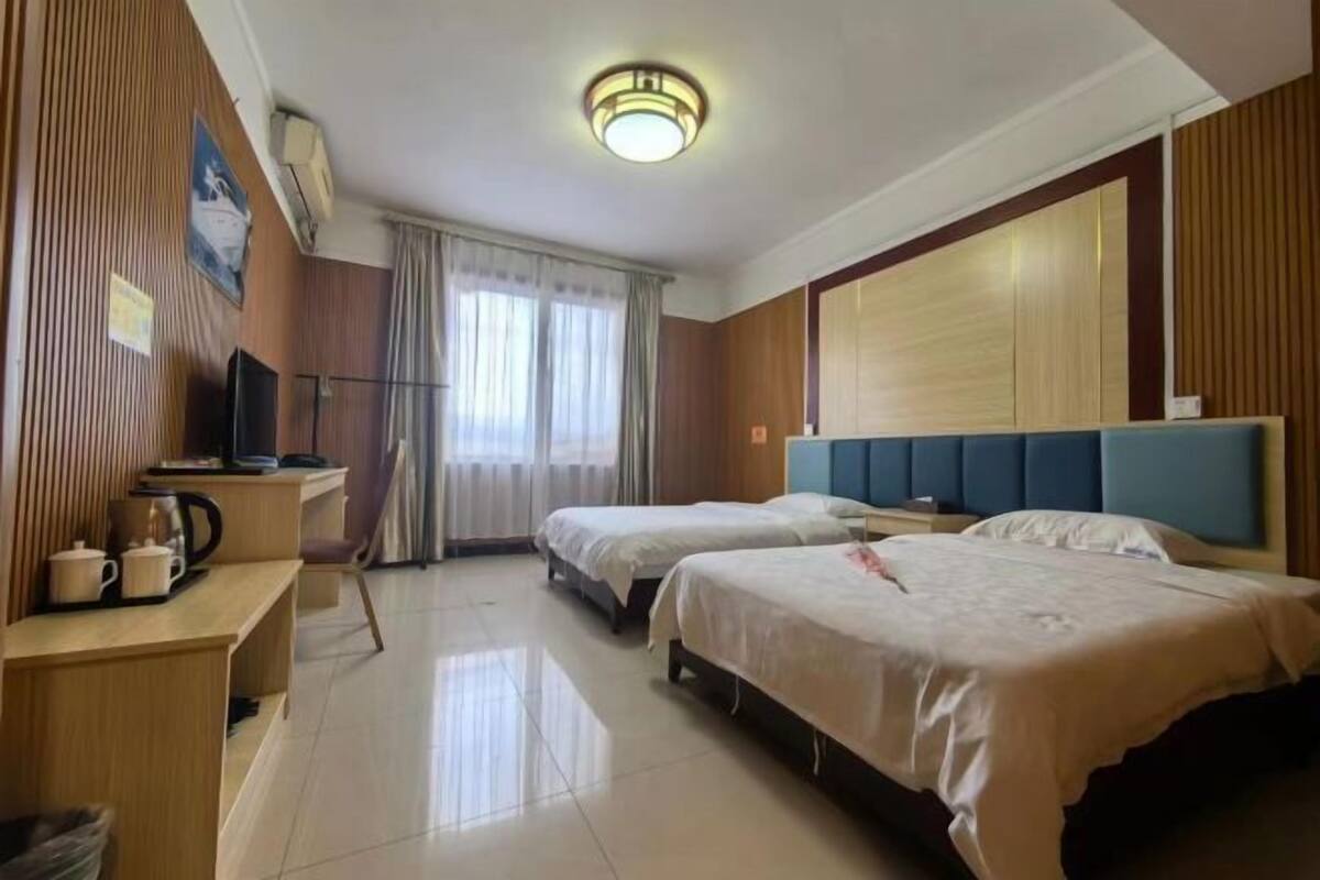 Une chambre d’hôtel avec deux lits, un bureau avec une chaise, une télévision et une fenêtre avec des rideaux.