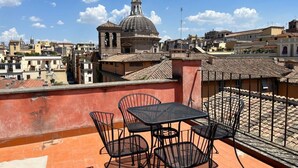 Terraço no telhado com mesa e cadeiras, vista para um horizonte urbano com edifícios históricos e uma cúpula imponente.