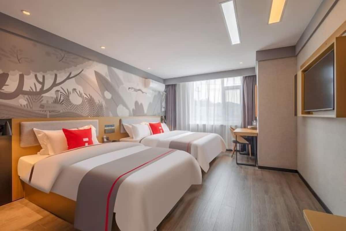 A hotel room with two beds, a desk, a TV, and a mural on the wall.