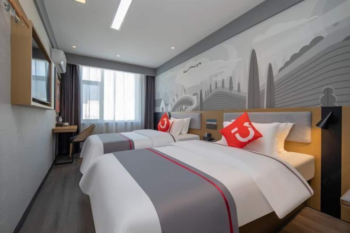 A hotel room with two beds, a desk, and a cityscape mural on the wall.