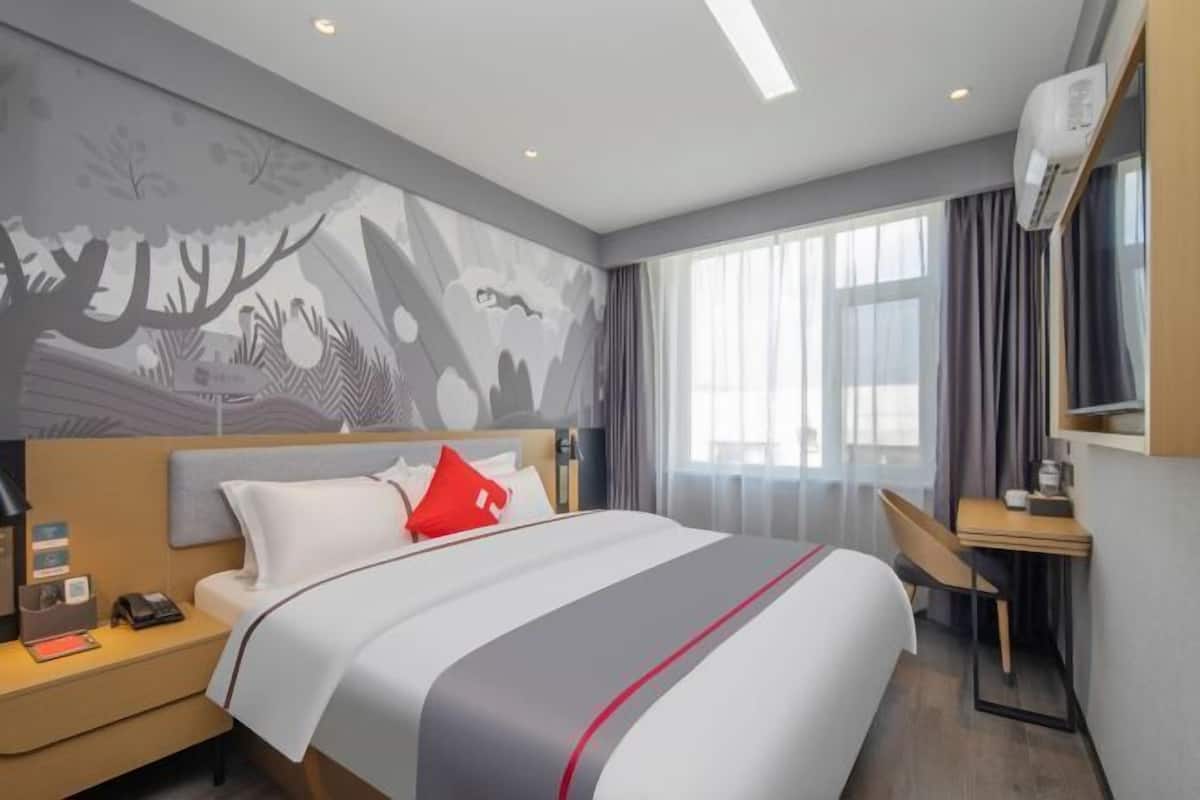 A modern hotel room with a large bed, a desk, and a wall mural.