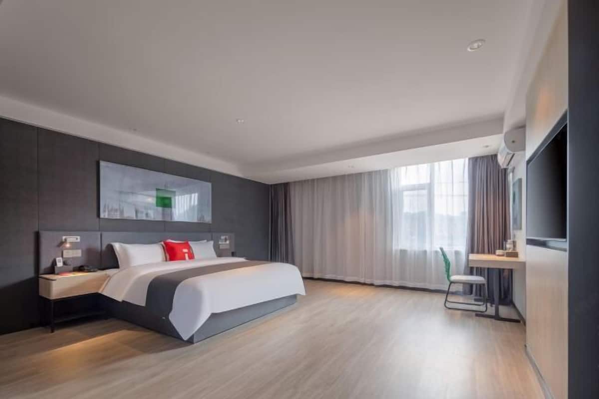 A modern hotel room with a large bed, a desk, and a television.