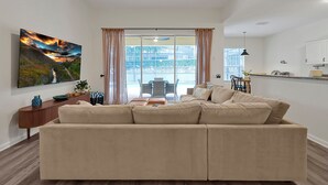Un salon moderne avec un canapé beige, un téléviseur à écran plat fixé au mur et une grande fenêtre avec des rideaux.