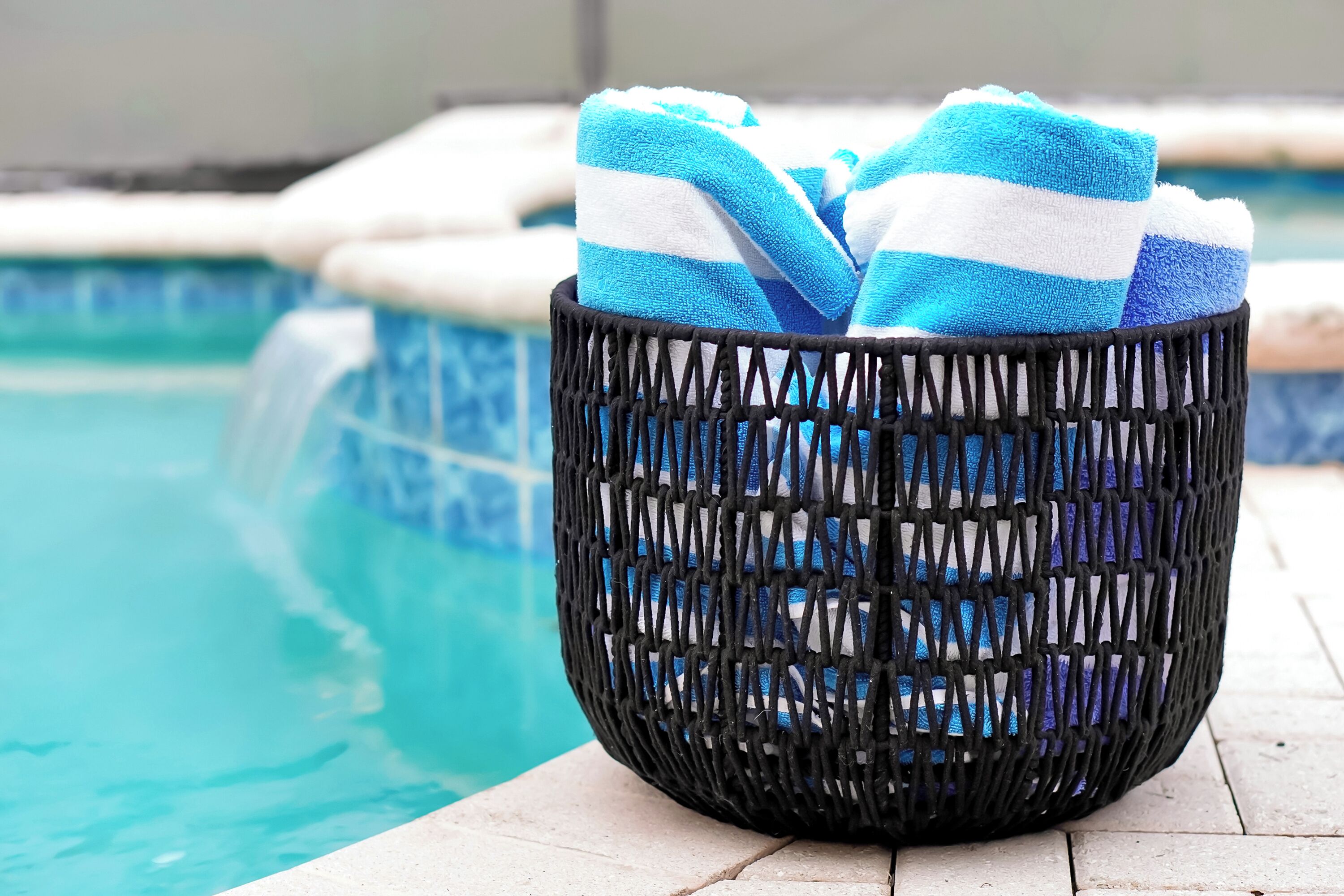 A wicker basket with blue and white striped towels on a poolside.