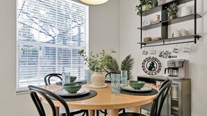 Un coin repas avec une table ronde en bois, des chaises noires et un bar à café avec des étagères au-dessus.