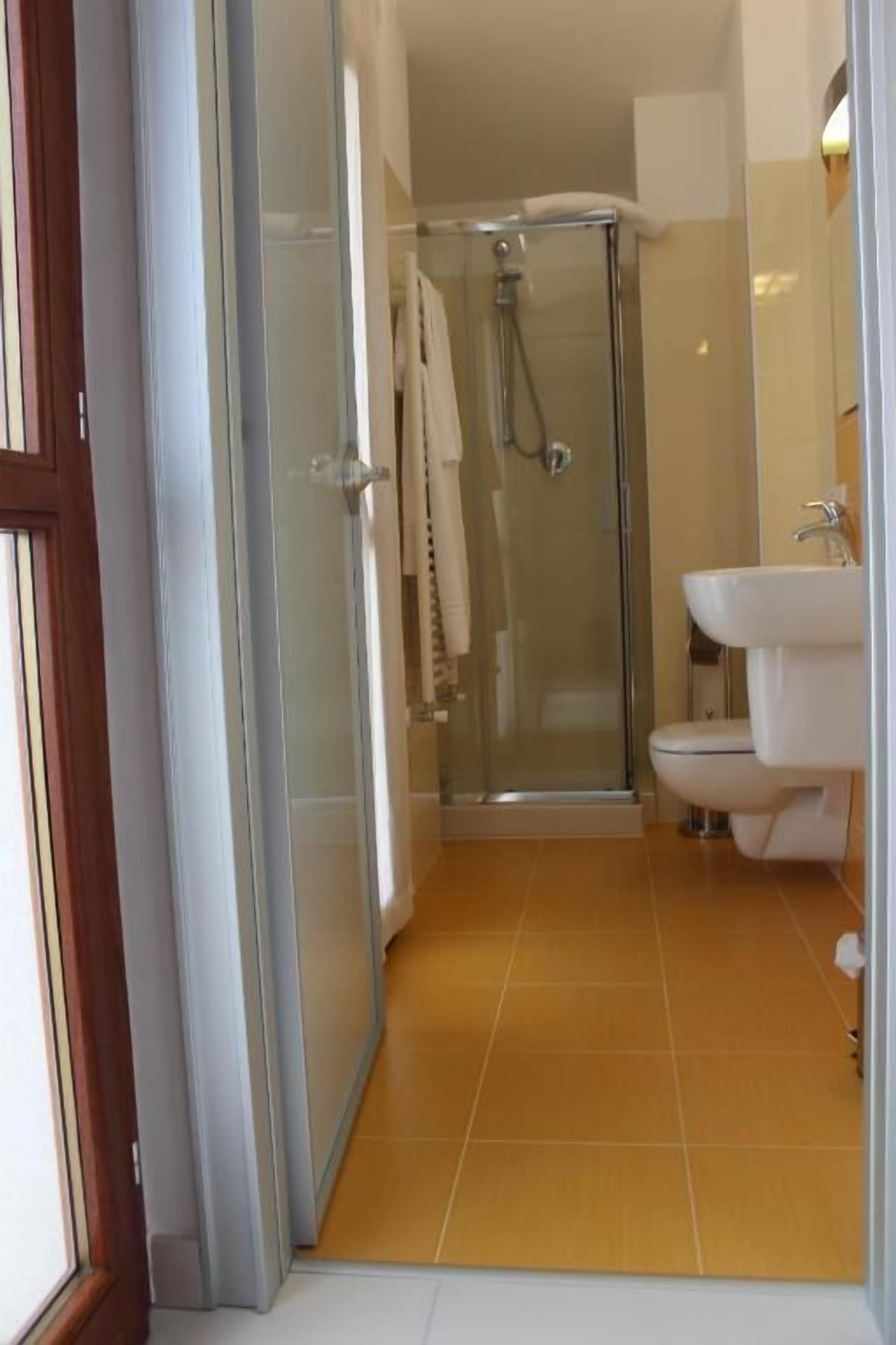 A bathroom with a glass shower enclosure, a white sink, and a tiled floor.