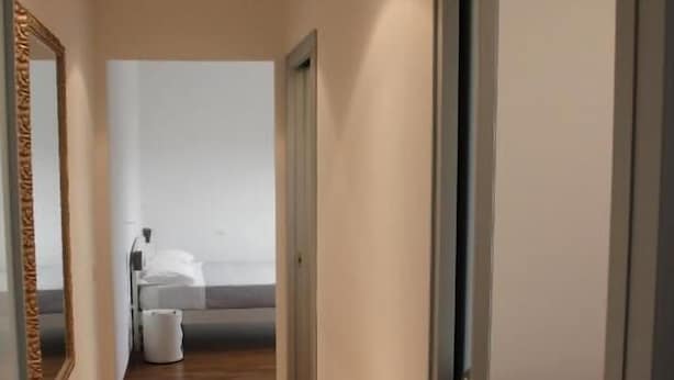 A narrow hallway with wooden flooring leading to a bedroom with a bed and a white trash bin. - B&B San Salvo (San Salvo)