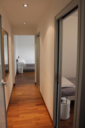 A narrow hallway with wooden flooring leading to a bedroom with a bed and a white trash bin. - B&B San Salvo (San Salvo)