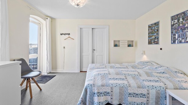 Een slaapkamer met een bed, een bureau, een stoel, een deur en een raam.