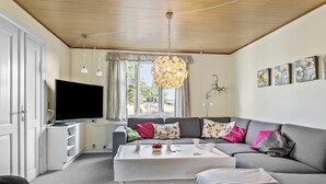 Een moderne woonkamer met een grijze bank, een witte salontafel en een flatscreen televisie op een witte kast.