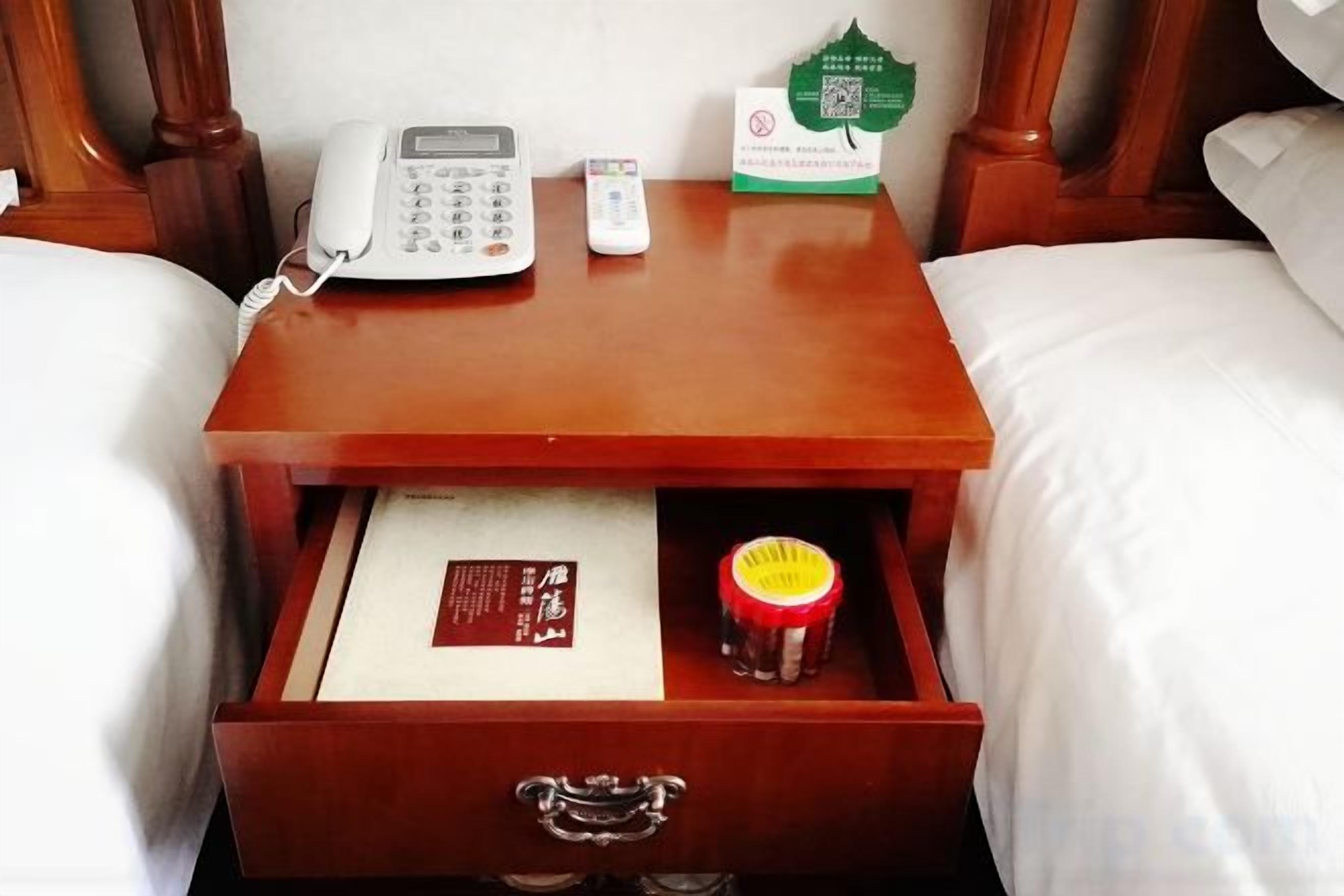A wooden bedside table with a white phone, a small container, and a card.