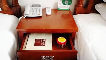 A wooden bedside table with a white phone, a small container, and a card.
