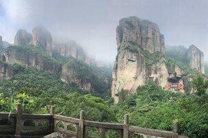 Un paisaje montañoso con un puente de madera y una estructura roja sobre un acantilado.