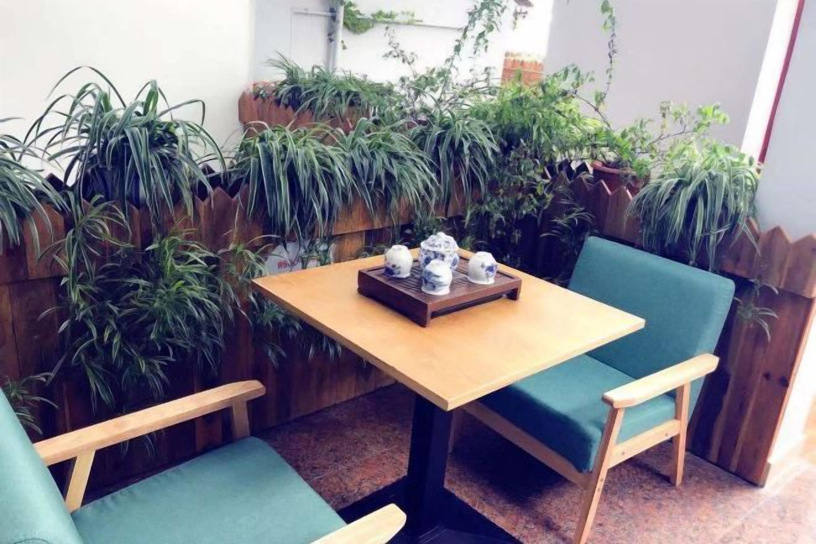 A small outdoor seating area with a wooden table and two green cushioned chairs.