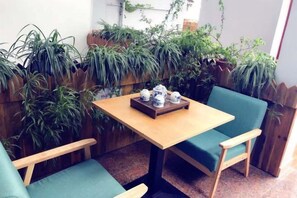 Un pequeño espacio al aire libre con una mesa de madera y dos sillas verdes con cojines.
