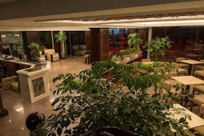 A hotel lobby with a reception desk, seating areas, and potted plants.