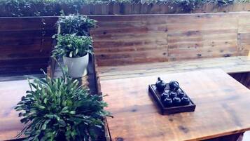 A wooden bench with potted plants, a table with a teapot, and a wooden railing with greenery.