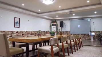 Un salón de conferencias con una larga mesa, sillas, una pantalla de proyector y un orador.