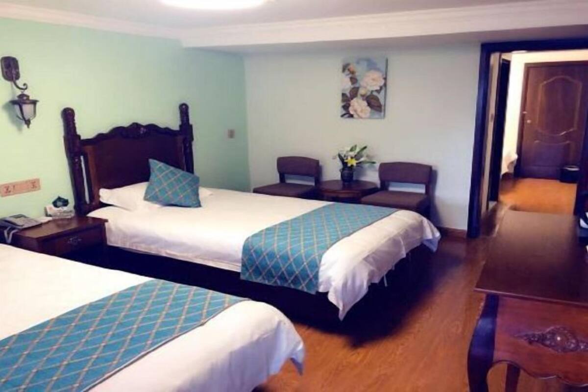 Habitación de hotel con dos camas, cabecera de madera, una mesita, dos sillas y un cuadro en la pared.