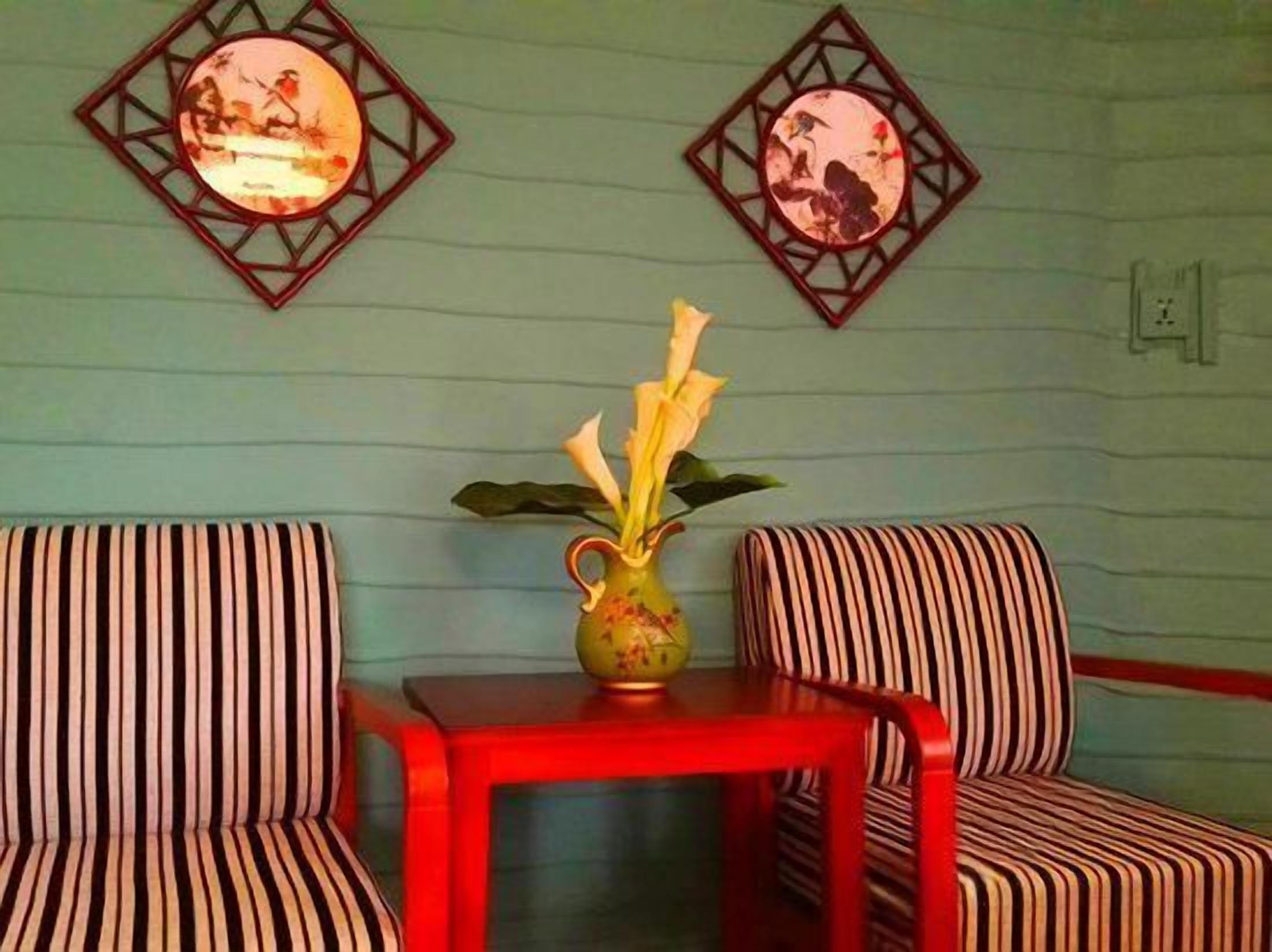 A room with striped chairs, a red table, and a vase with flowers.