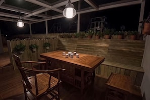An outdoor patio with a wooden table and chairs, potted plants, and hanging lights.