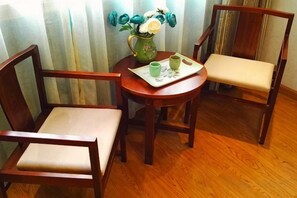 A room with two wooden chairs, a small round table with a vase of flowers, and a tray with a cup and saucer. - Yujian Duxiulou Hotel (Yueqing)