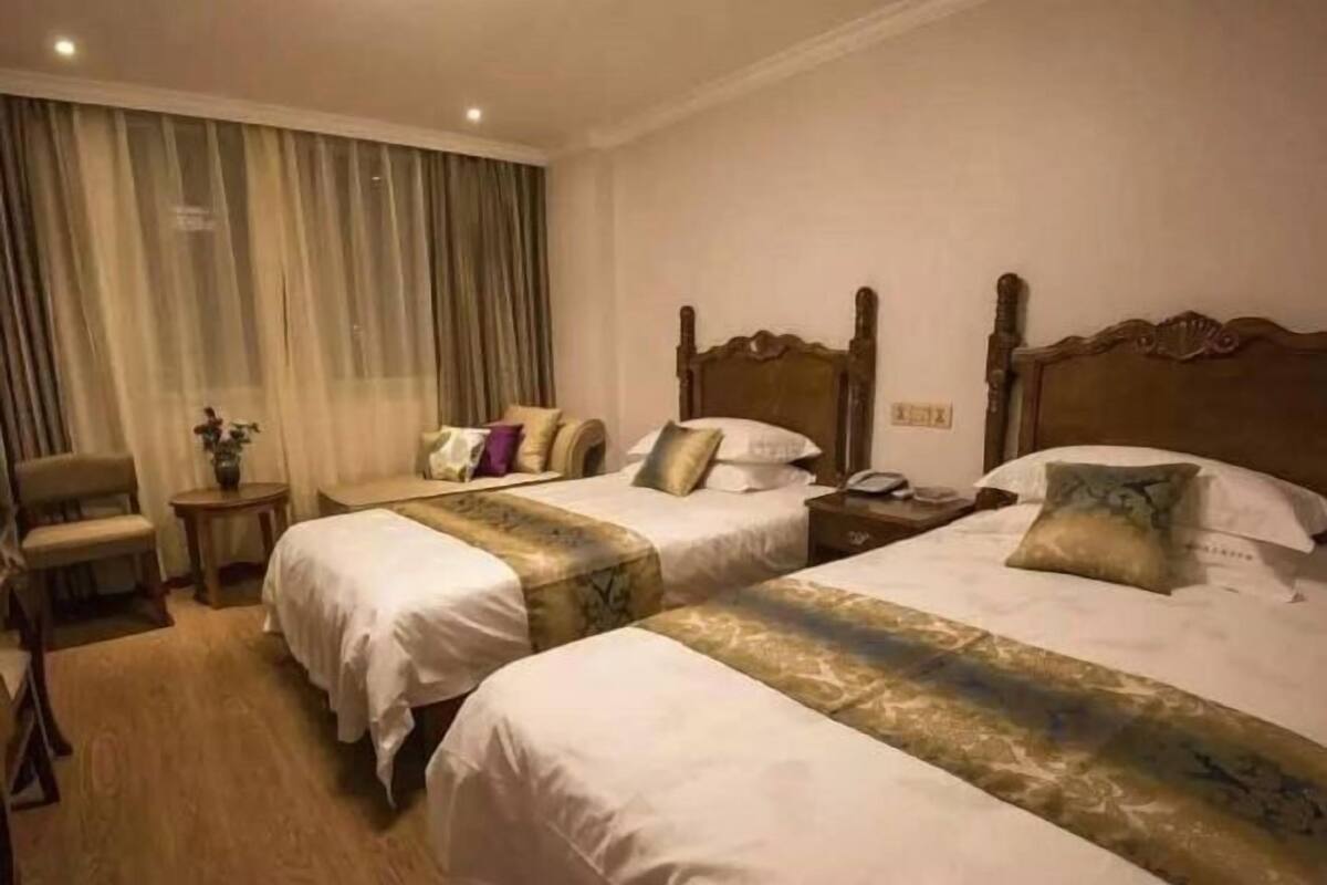 Habitación de hotel con dos camas, una silla, una mesita y una cortina.
