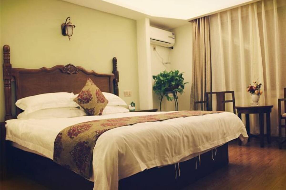 Una cama bien hecha con un cabecero de madera, una mesita de noche con una lámpara y una planta en maceta.