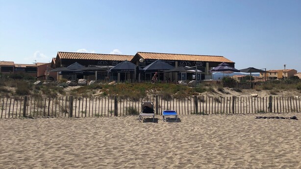 Ein Strandgrundstück mit einer Reihe von Villen direkt am Strand, jede mit einem Ziegeldach und einer überdachten Terrasse.