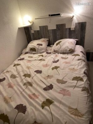 Sängyssä on kukkakuviollinen päiväpeite ja puinen pääty.