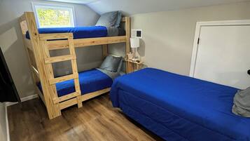 Habitación tipo dormitorio con literas, una ventana, un escritorio con lámpara y una puerta.